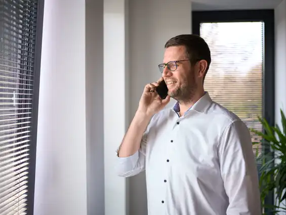 Ein Mitarbeiter, der vor einem Fenster steht und telefoniert.