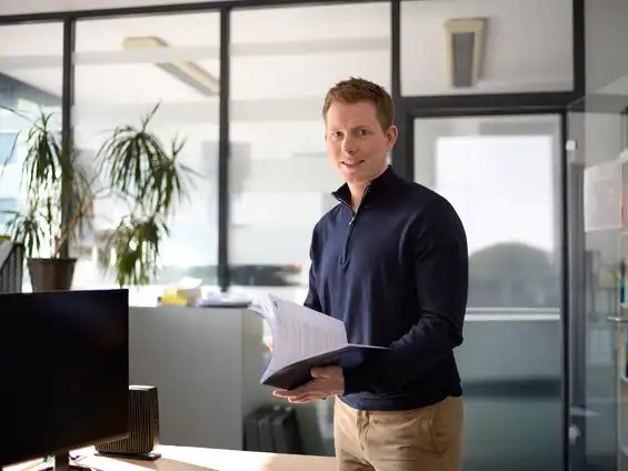 Ein Mann steht in einem Büro und hält Unterlagen in den Händen